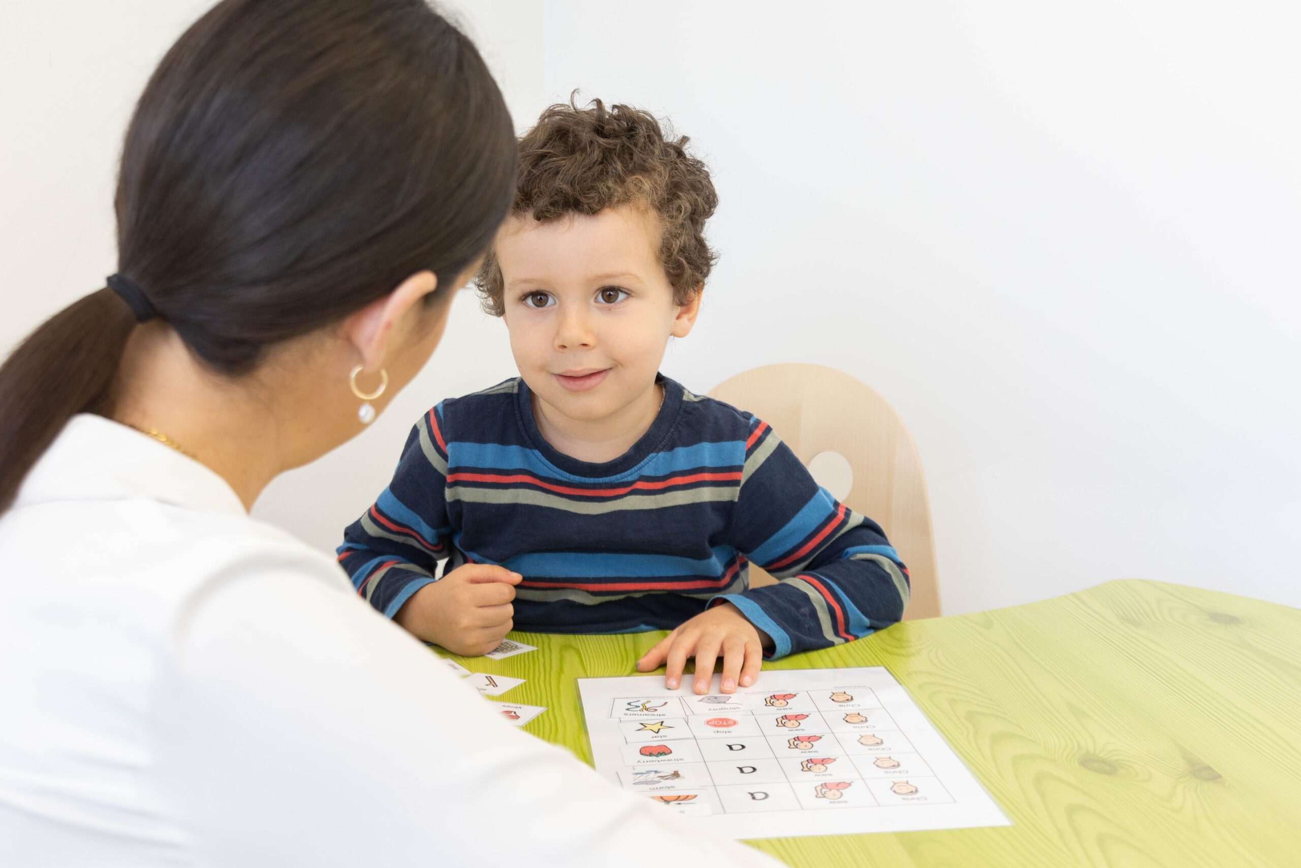 Boy looks attentively at a woman while completing a worksheet at a table.