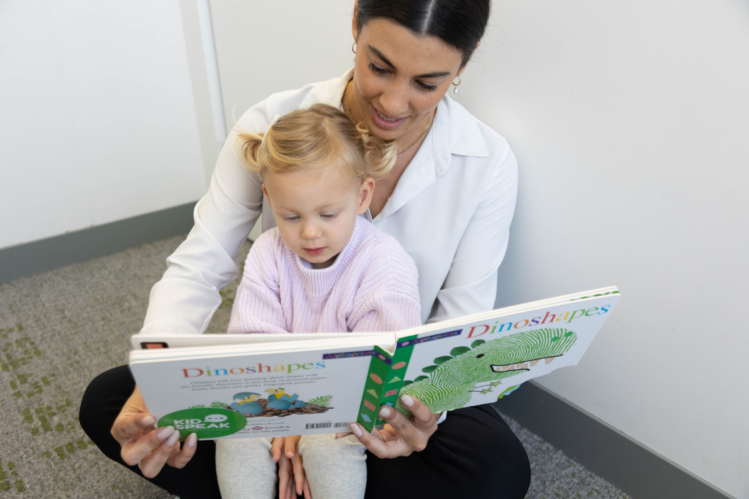 Woman reads a book to a young girl seated on her lap.