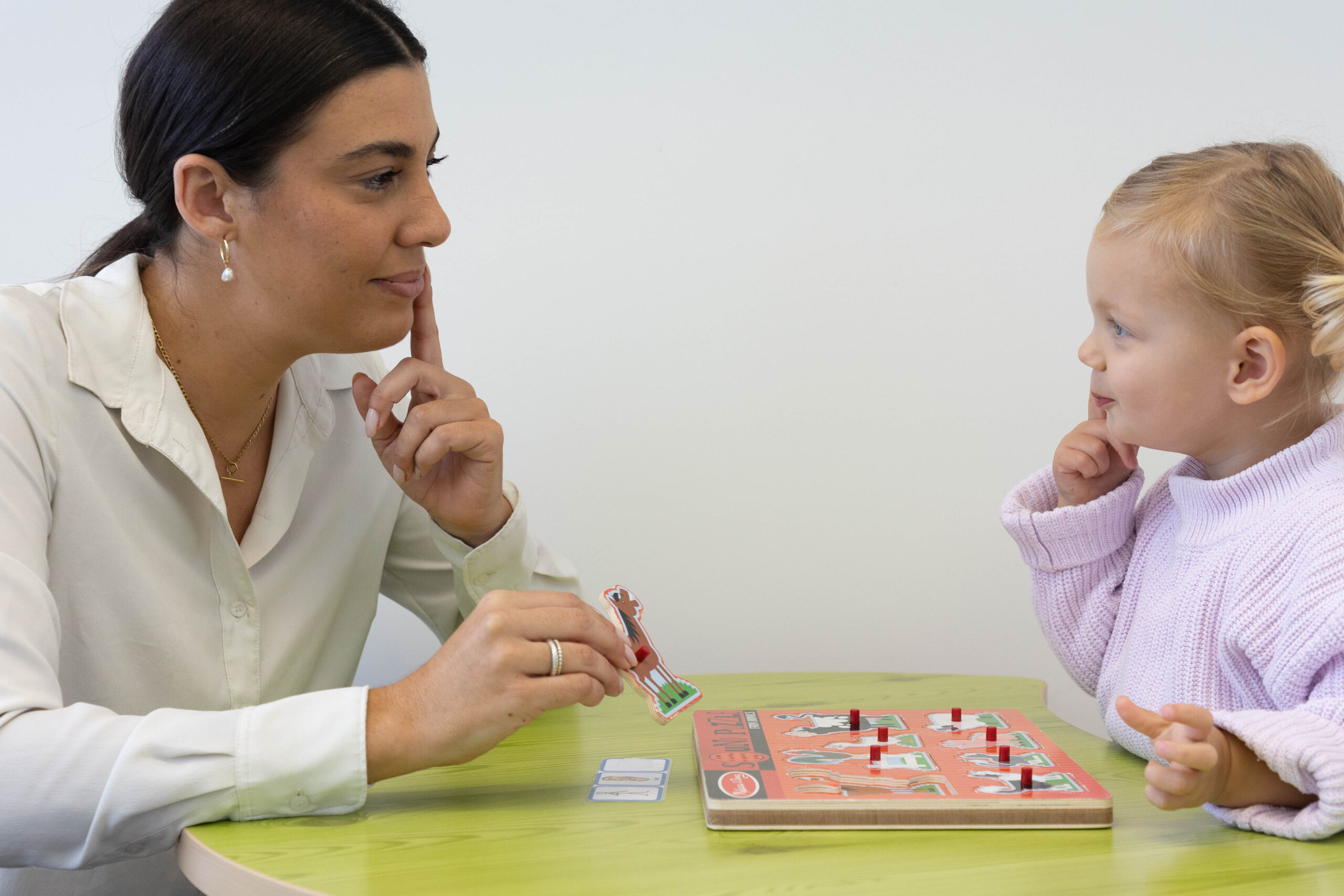 Woman and a girl playing with a puzzle while touching their chins thoughtfully.