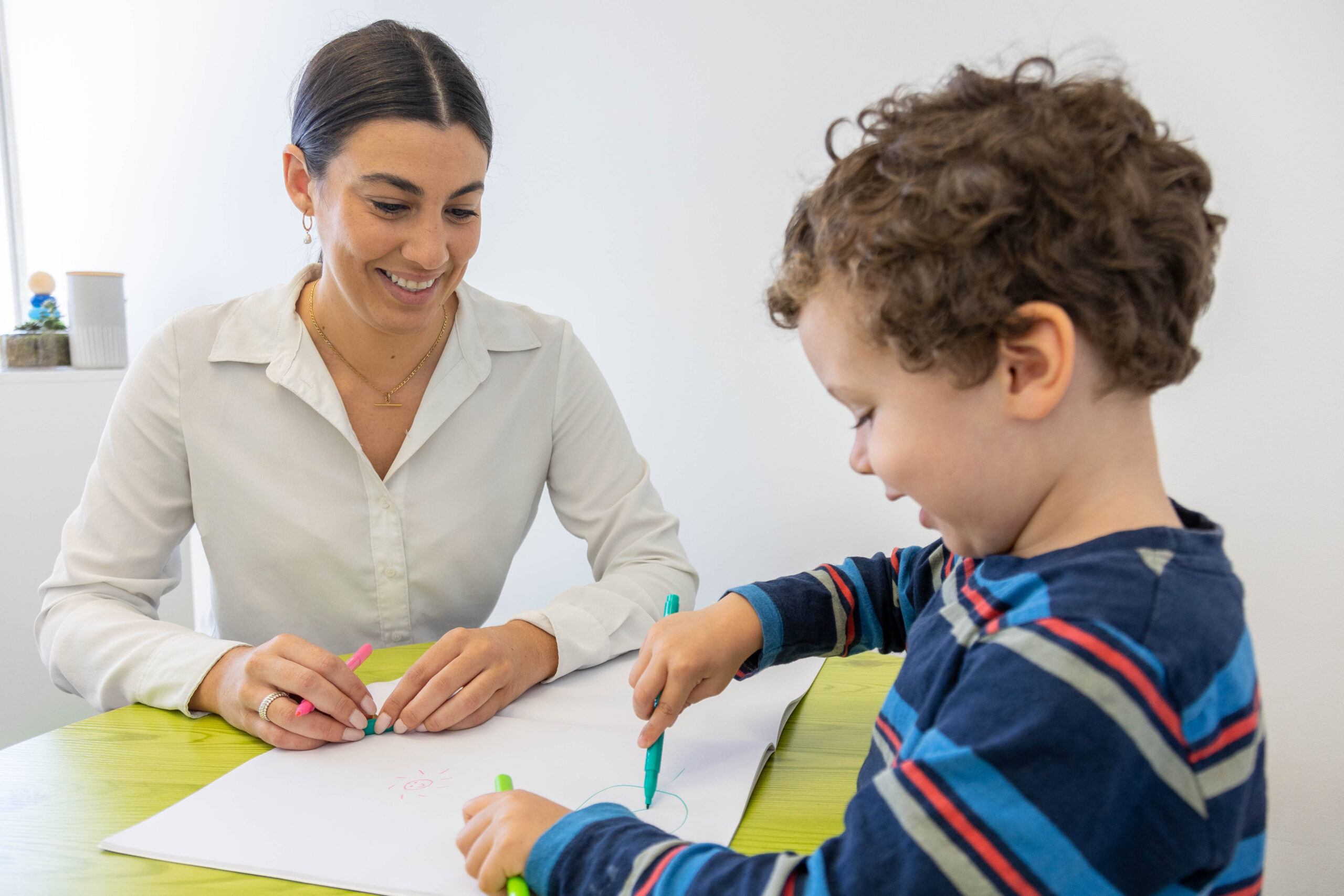 A woman and a child happily draw together at a table using colorful markers.